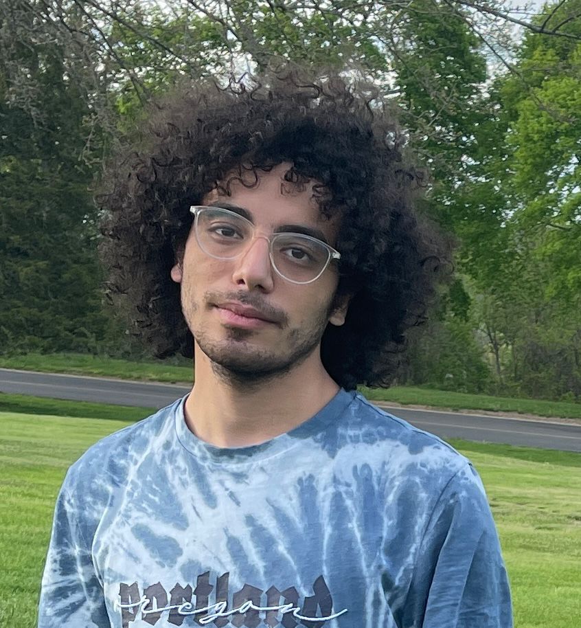 A young man with curly hair and a tie-dyed shirt.